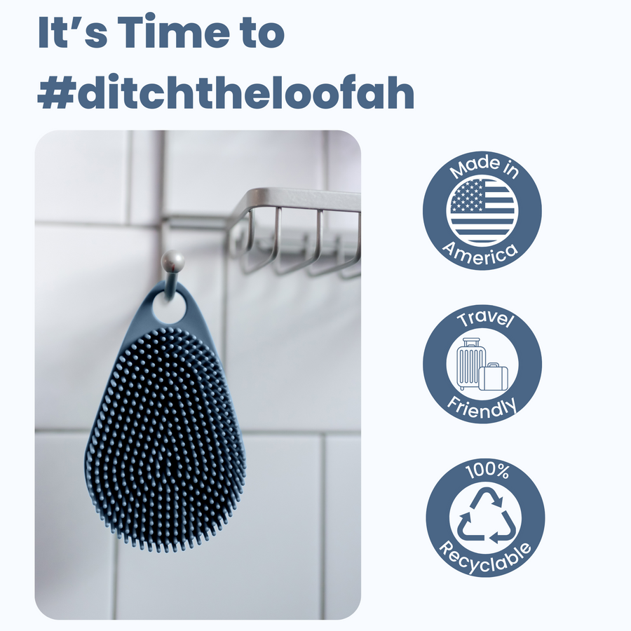 A black Scalp and Body Scrubber with gentle bristles hangs on a hook in a tiled bathroom, accompanied by icons highlighting it being American-made, travel-friendly, and 100% recyclable.
