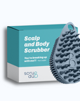 A blue silicone exfoliating brush is displayed in front of its teal and white packaging, which reads "The scrub-dub® Scalp and Body Scrubber" and "You're breaking up with me?! – Your Loofah." The brand name, Scrub-dub®, is located at the bottom.