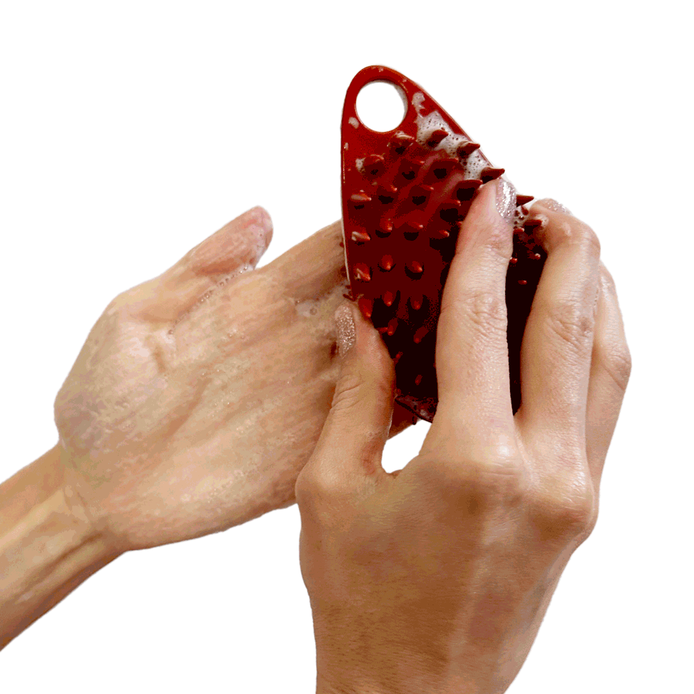 Hand holding body scrubber sliding it back and forth in hand with soap to make bubbles.