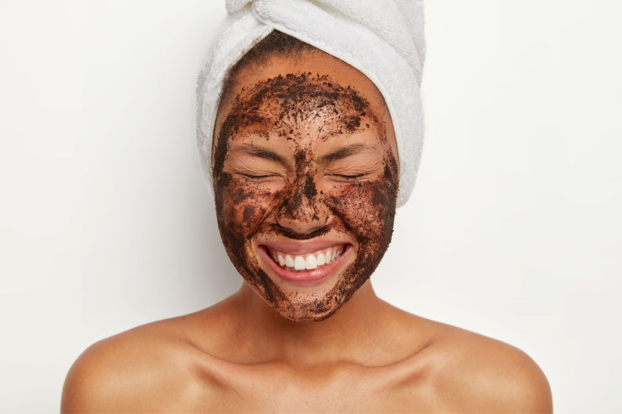 Woman with coffee body scrub on her face smiling.
