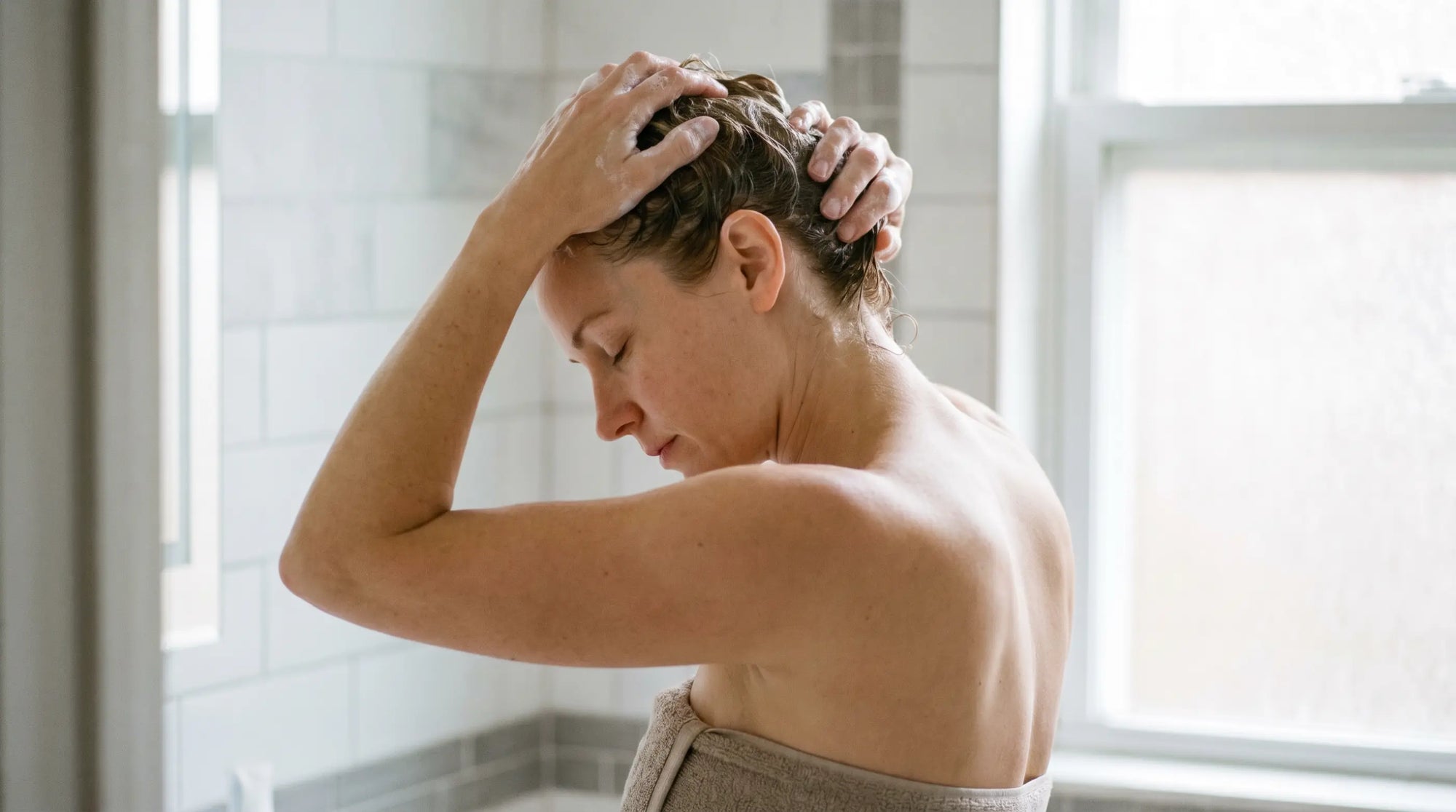Woman working shampoo lather into her wet scalp to treat dandruff