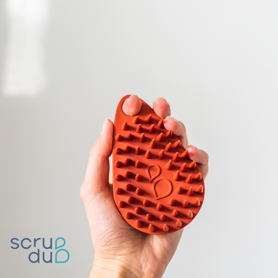 A person holding a Scalp and Body Scrubber - Sedona Red brush in their hand, perfect for their skincare needs.