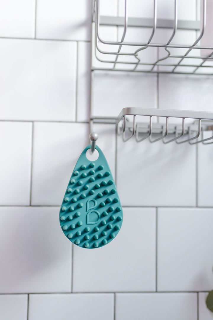 Silicone body scrubber hangs from hanging hook in shower to dry.