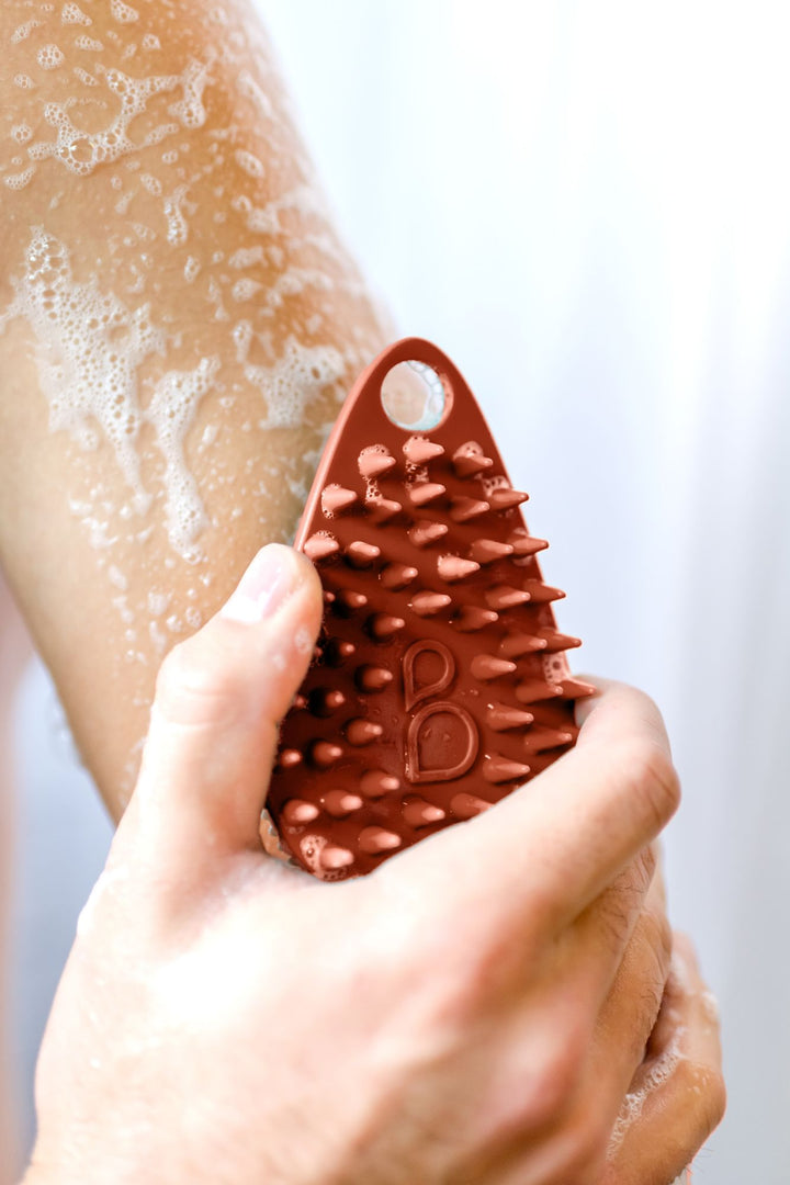 Man holds silicone body scrubber to lather body with silicon body bristles.