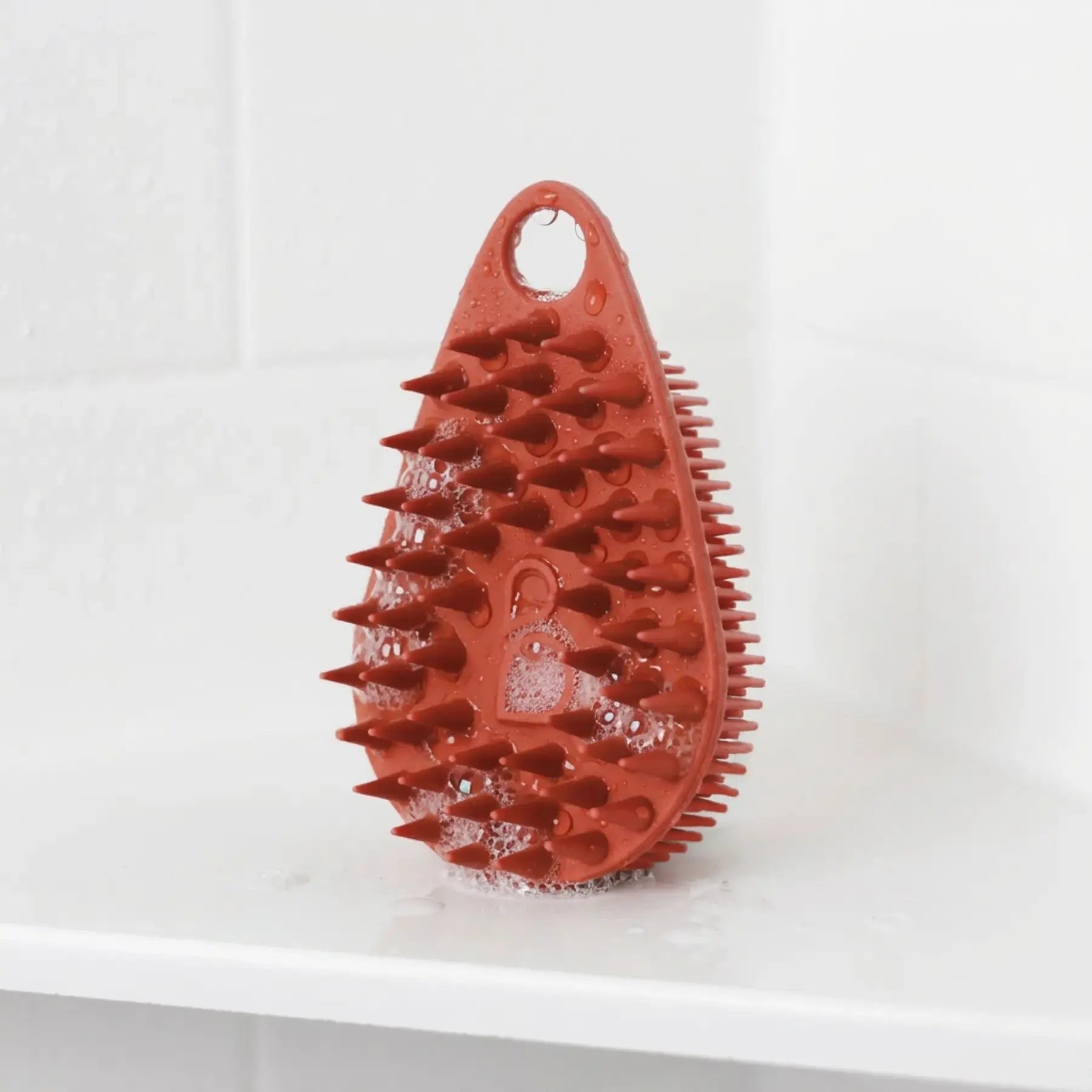 Scrub-Dub® scalp scrubber in red, designed to remove dandruff and buildup, shown with water droplets.