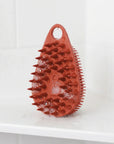 Scrub-Dub® scalp scrubber in red, designed to remove dandruff and buildup, shown with water droplets.
